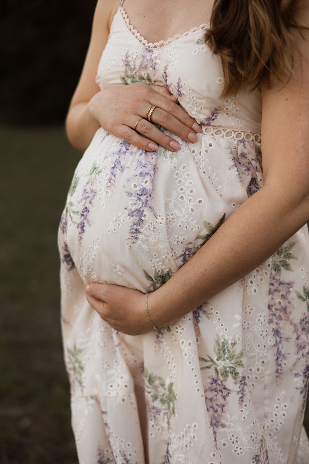 Close-up view of a pregnant belly in a white floral dress with delicate purple floral details and eyelet lace pattern.