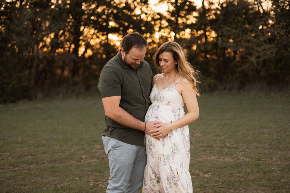 A couple shares an intimate moment in a field during sunset as they celebrate an upcoming arrival.