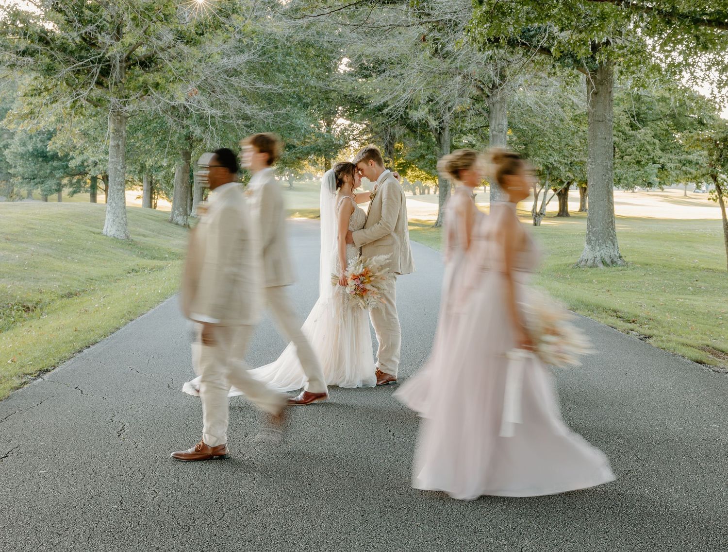 Wedding party walks along a tree-lined path in soft pastel dresses creating an ethereal motion blur effect.