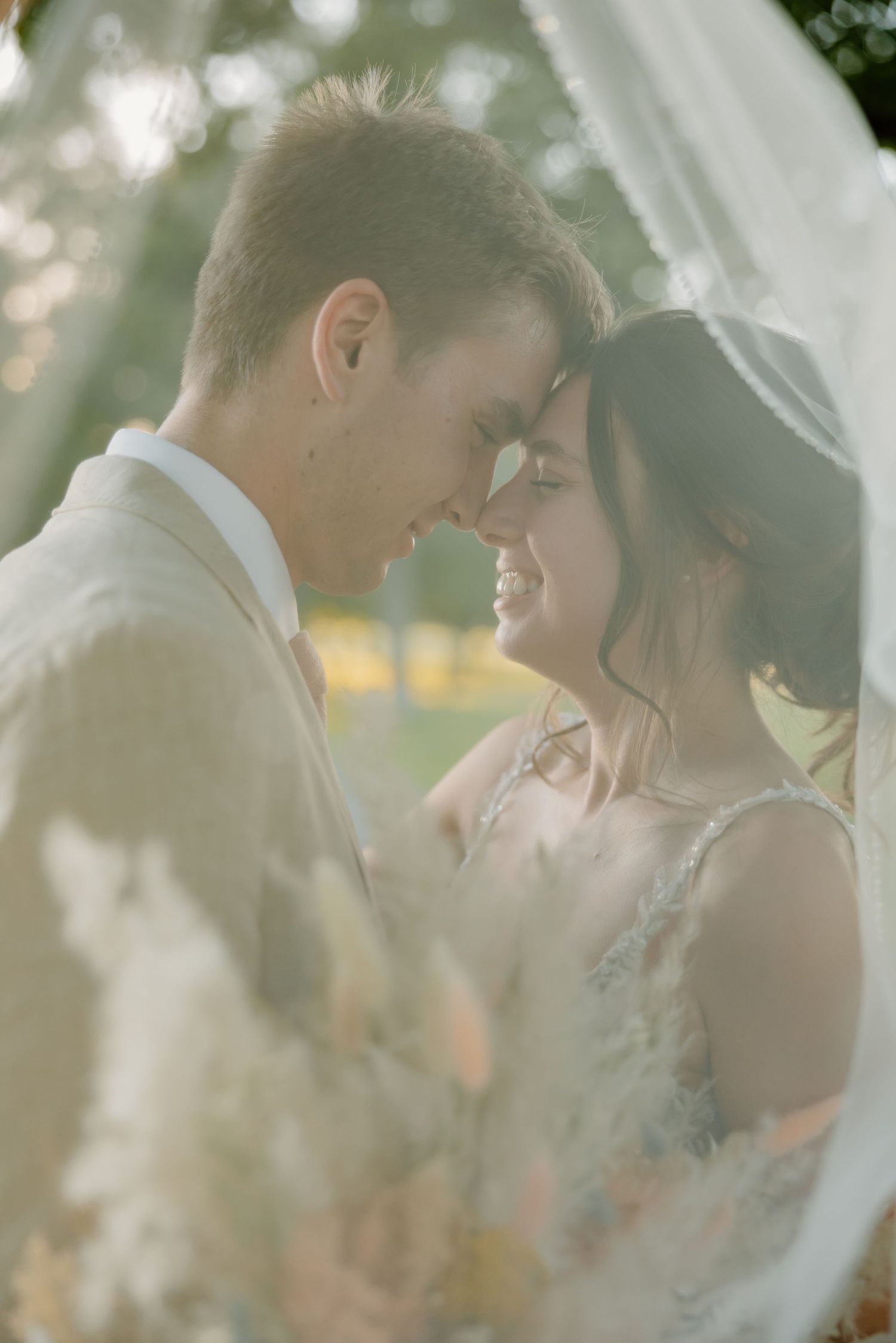 Romantic wedding couple shares an intimate moment under soft sunlight and veil.