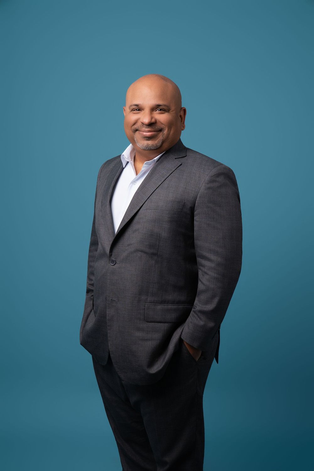 Professional headshot of someone in a dark suit jacket against a teal blue background.