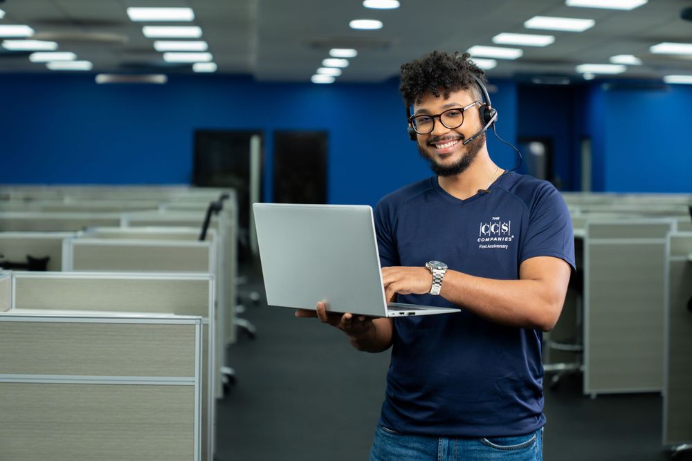 Tech professional smiling while holding laptop in office environment.