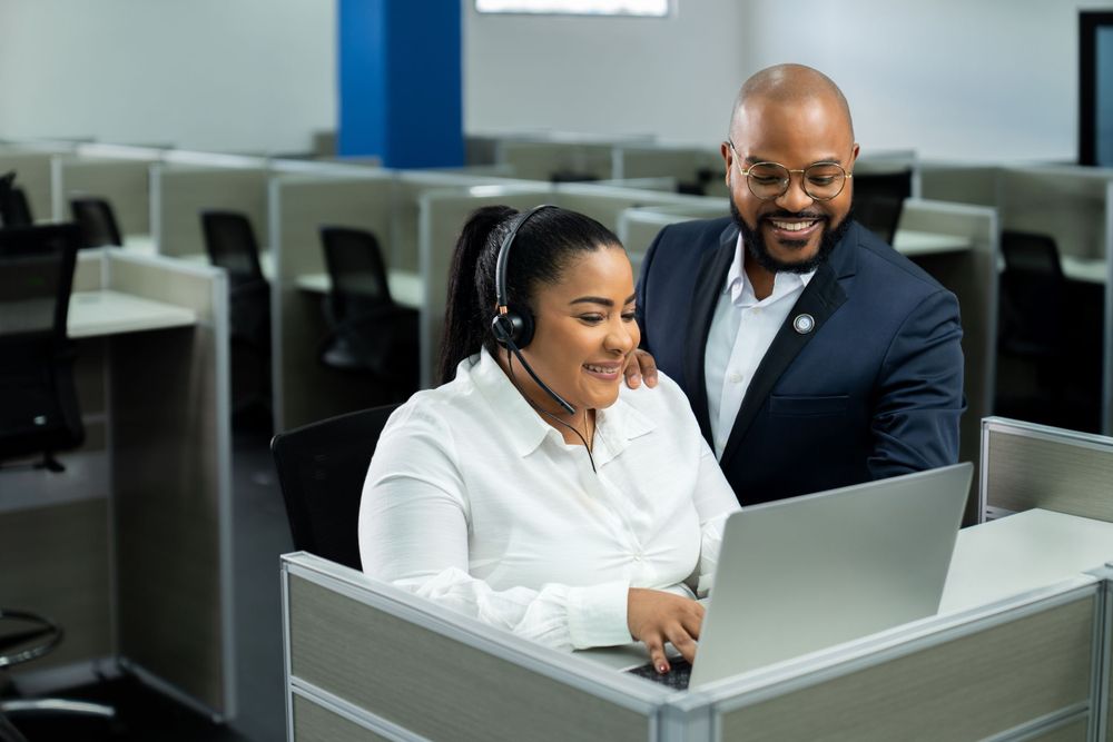 Professional colleagues collaborating on a laptop in a modern office call center setting.