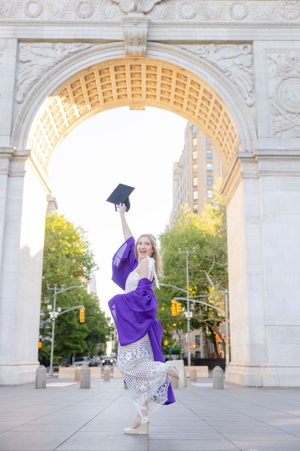 Graduate celebrates under arch while jumping and holding graduation cap.
