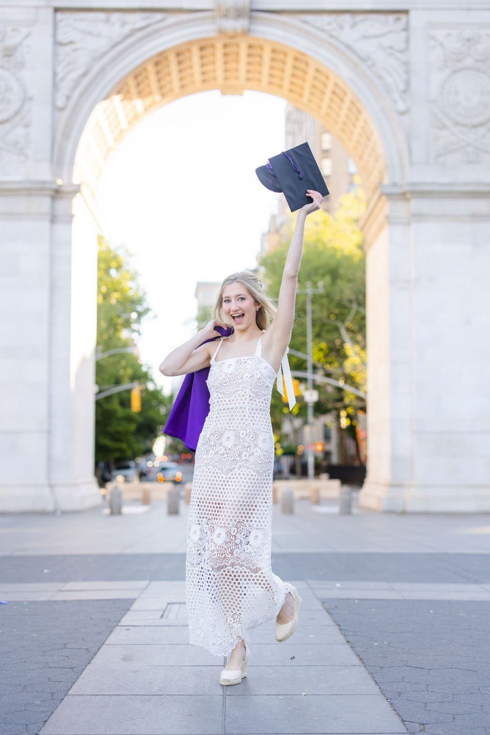 Graduate celebrates with cap toss under historic stone arch.