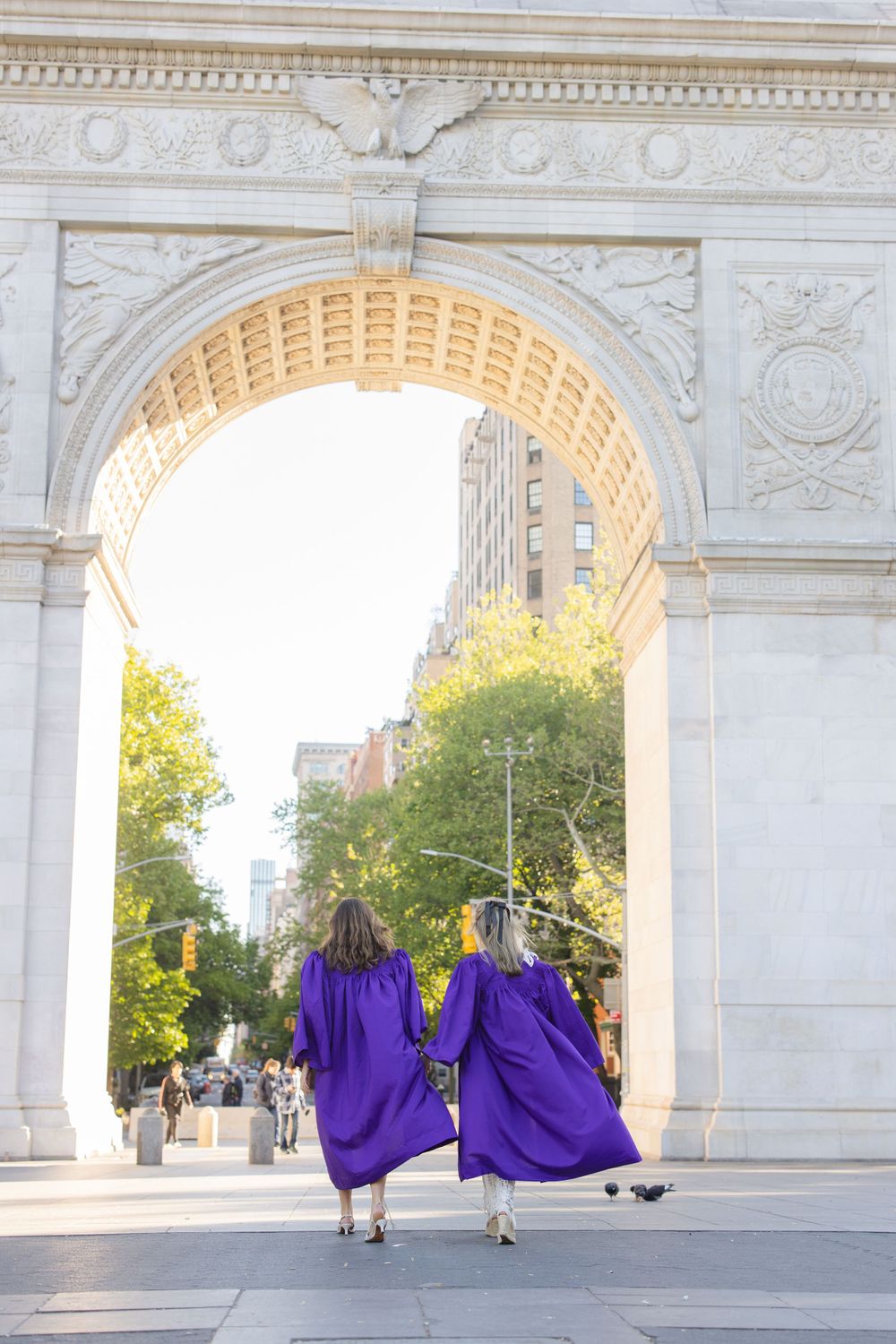 Two graduates in purple robes walk through Washington Square Arch together.