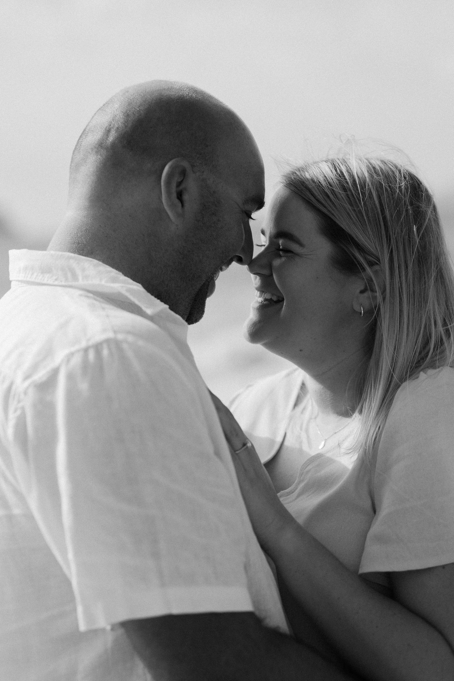 A romantic black and white portrait of a couple sharing an intimate moment as they smile close together.