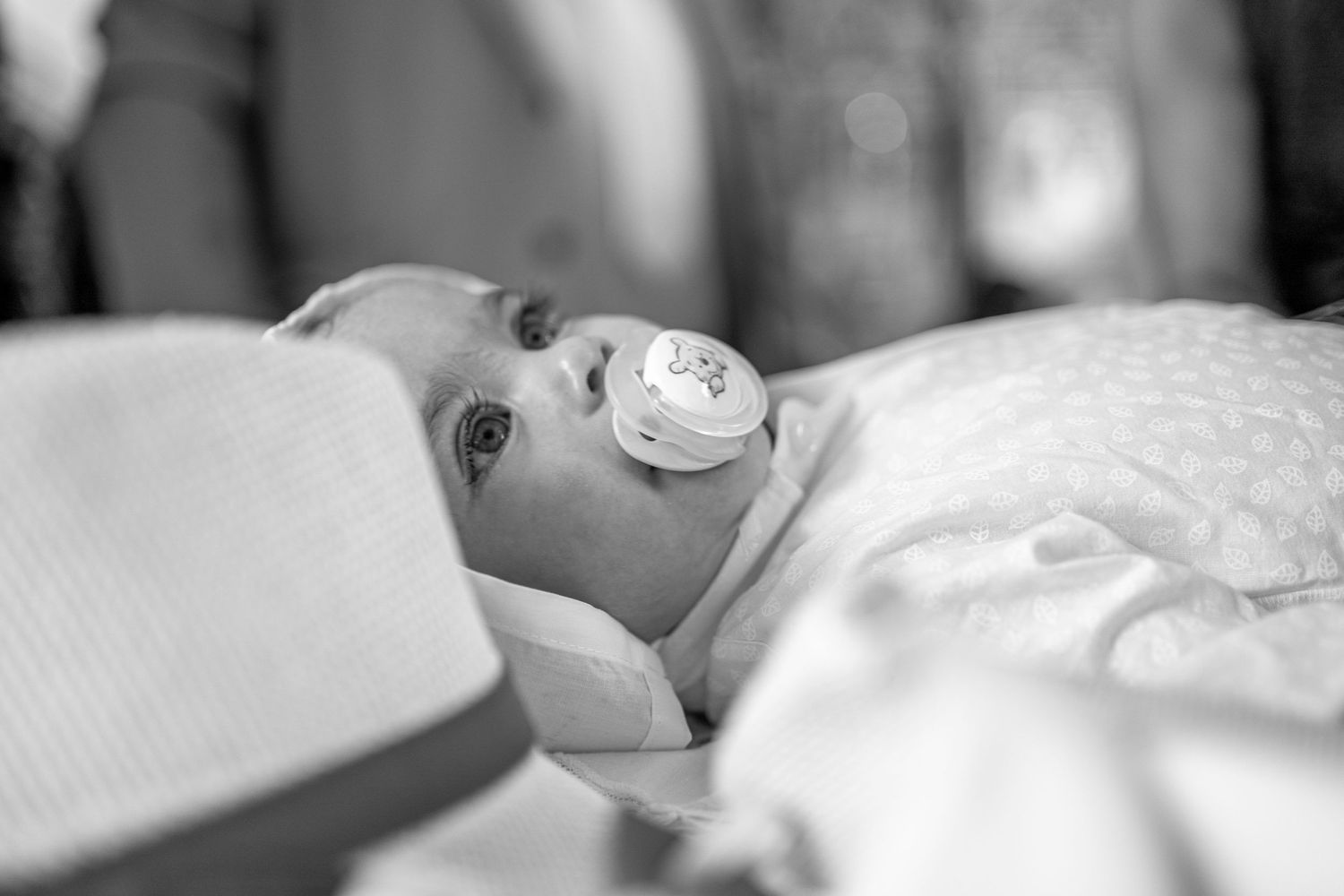 Black and white photo of a peaceful baby with a pacifier resting on white bedding.
