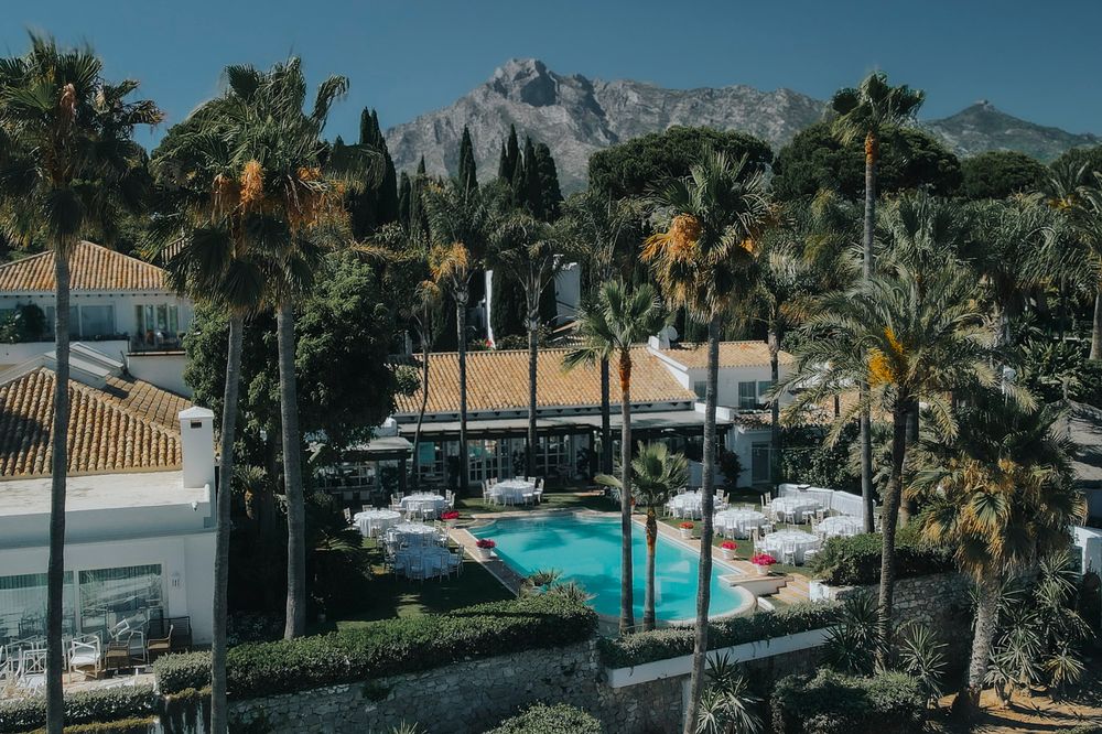 Luxury resort pool surrounded by palm trees with mountain peaks rising dramatically in background near Marbella, Spain.