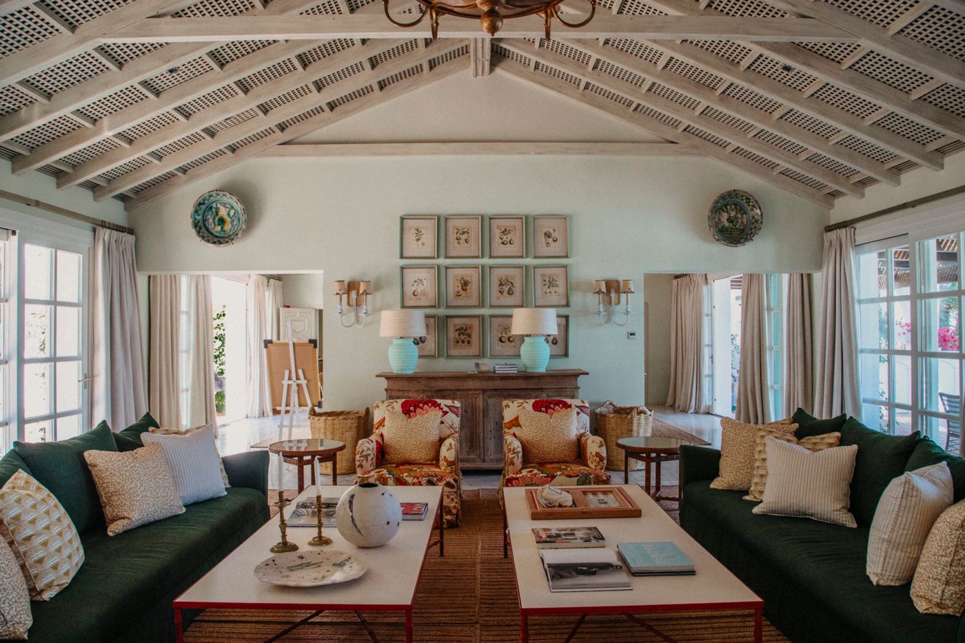 Cozy coastal living room with vaulted white ceiling, green velvet sofas, and vintage art gallery wall in soft blue-green tones.