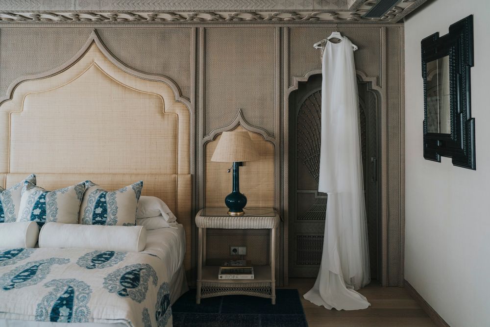 Elegant bedroom interior with moroccan-style headboard, blue floral bedding, and white wedding dress hanging on display.