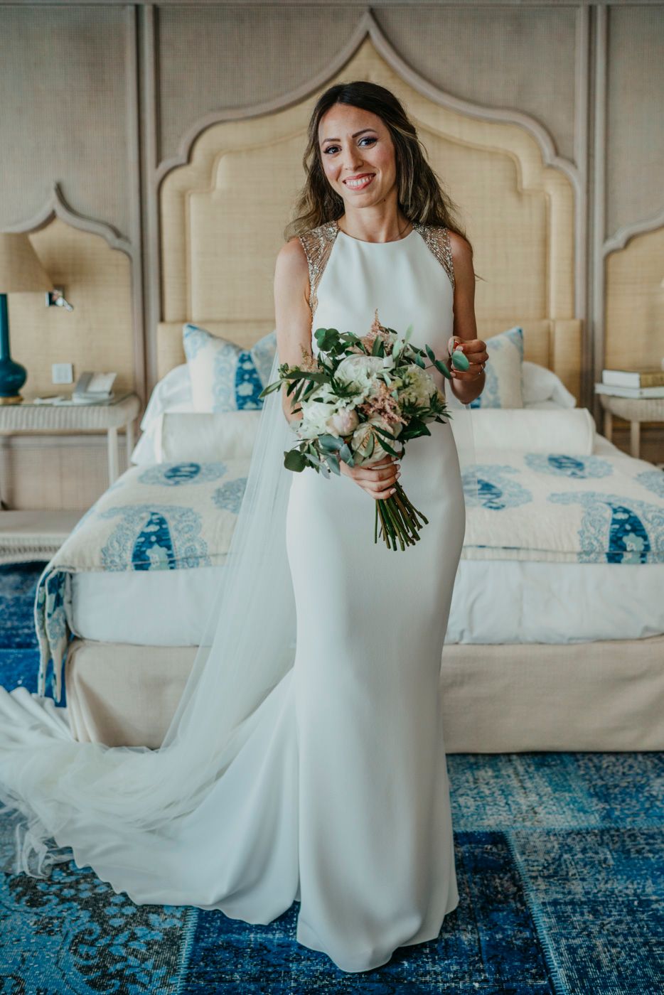 A white wedding dress against an elegant bedroom backdrop with blue accents and a decorative headboard.