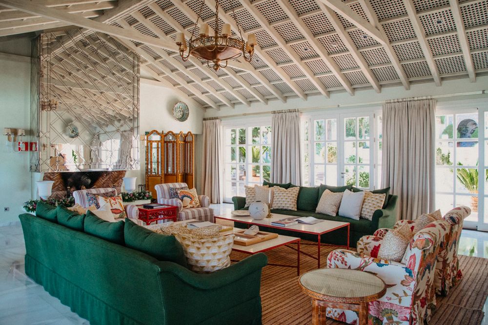 Coastal living room with exposed beam ceiling, emerald green sofa and rustic chandelier in a beach house setting.