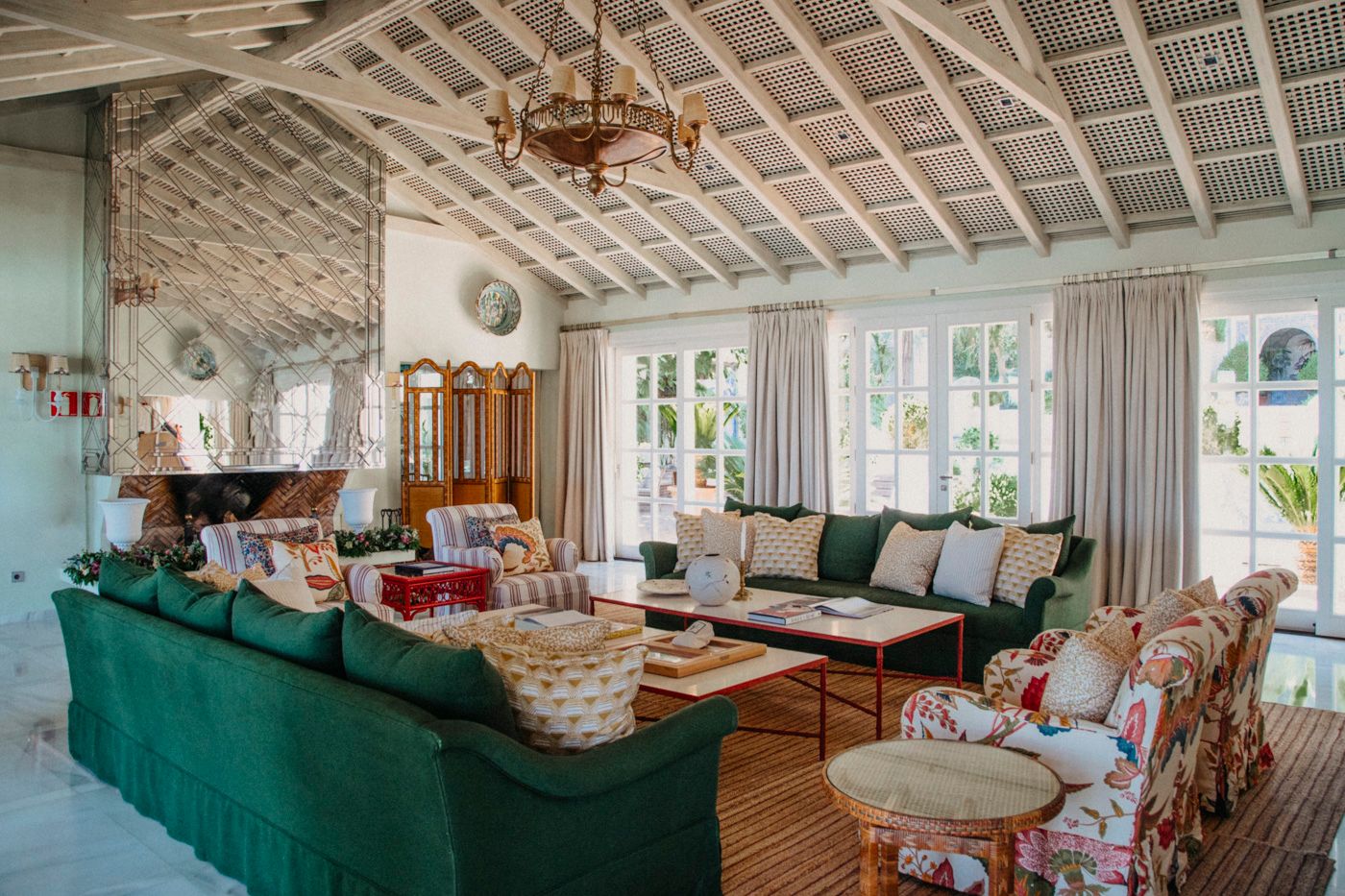Coastal living room with exposed beam ceiling, emerald green sofa and rustic chandelier in a beach house setting.