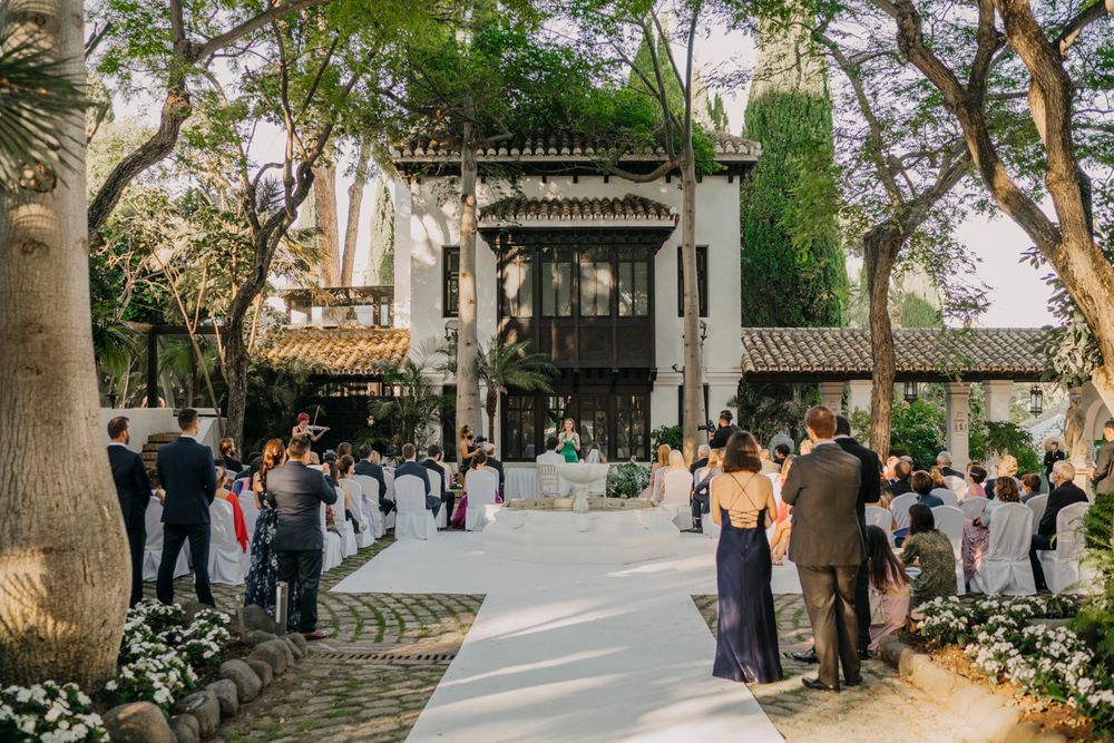 Guests gather outside an elegant Spanish Colonial style wedding venue entrance with ornate architectural details and lush landscaping.