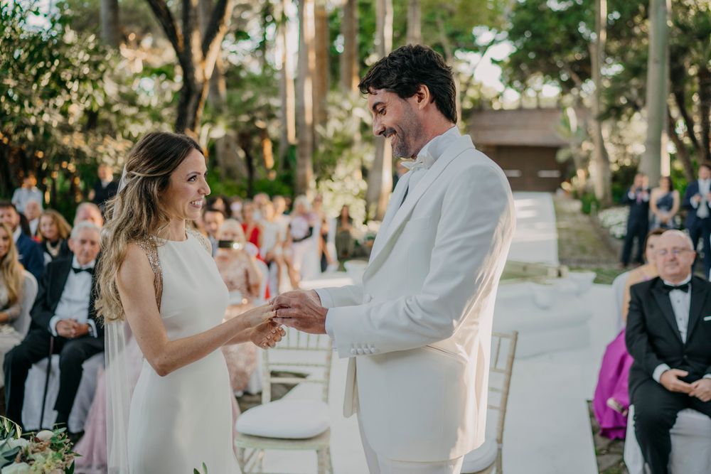 A romantic outdoor wedding ceremony with a couple exchanging rings in front of gathered guests in a garden setting.