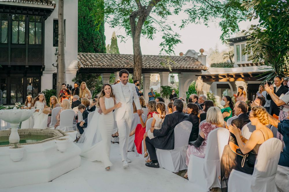 Wedding guests celebrate and take photos during an outdoor reception at a rustic venue with garden surroundings.