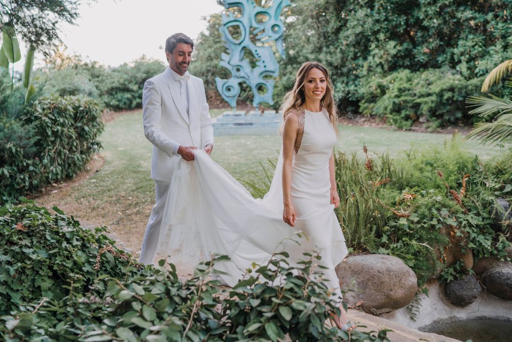 Wedding couple poses together in a lush garden setting with greenery and a blue sculpture in the background.