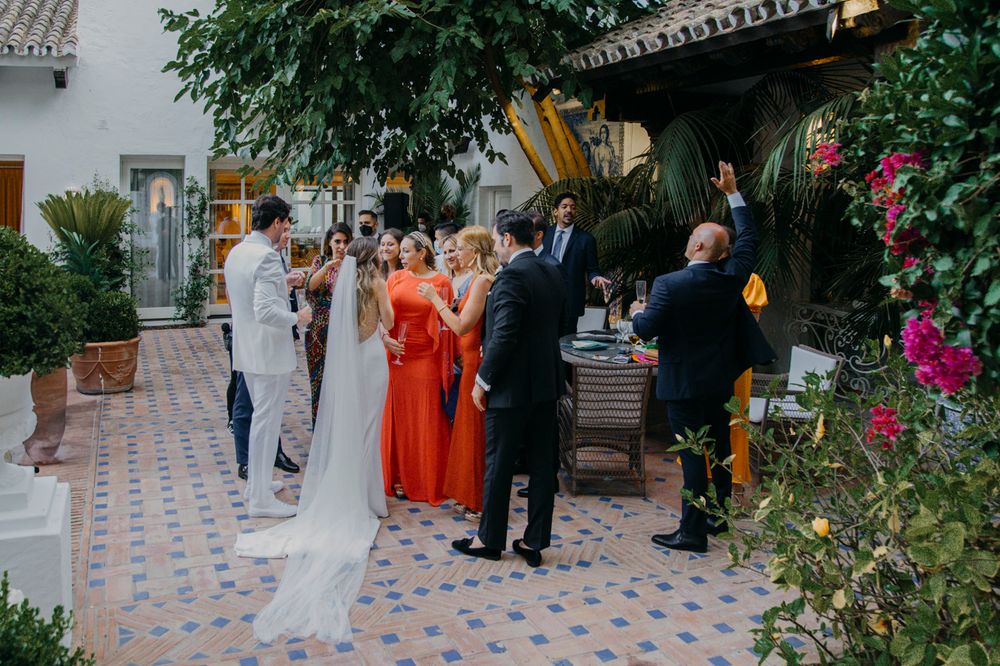 Guests gather on a tiled courtyard patio surrounded by flowers and Spanish-style architecture during a celebration.