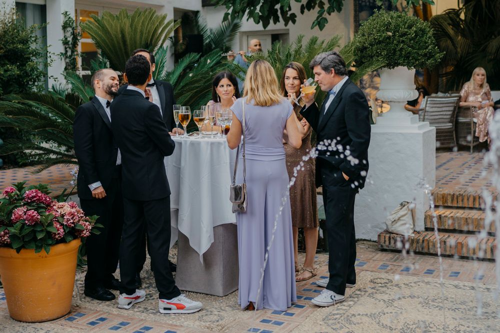 Guests in formal attire gather around cocktail tables at an elegant outdoor garden reception.
