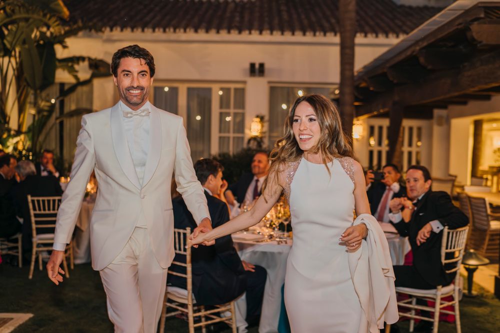 A wedding couple dances together at their outdoor evening reception while guests look on.