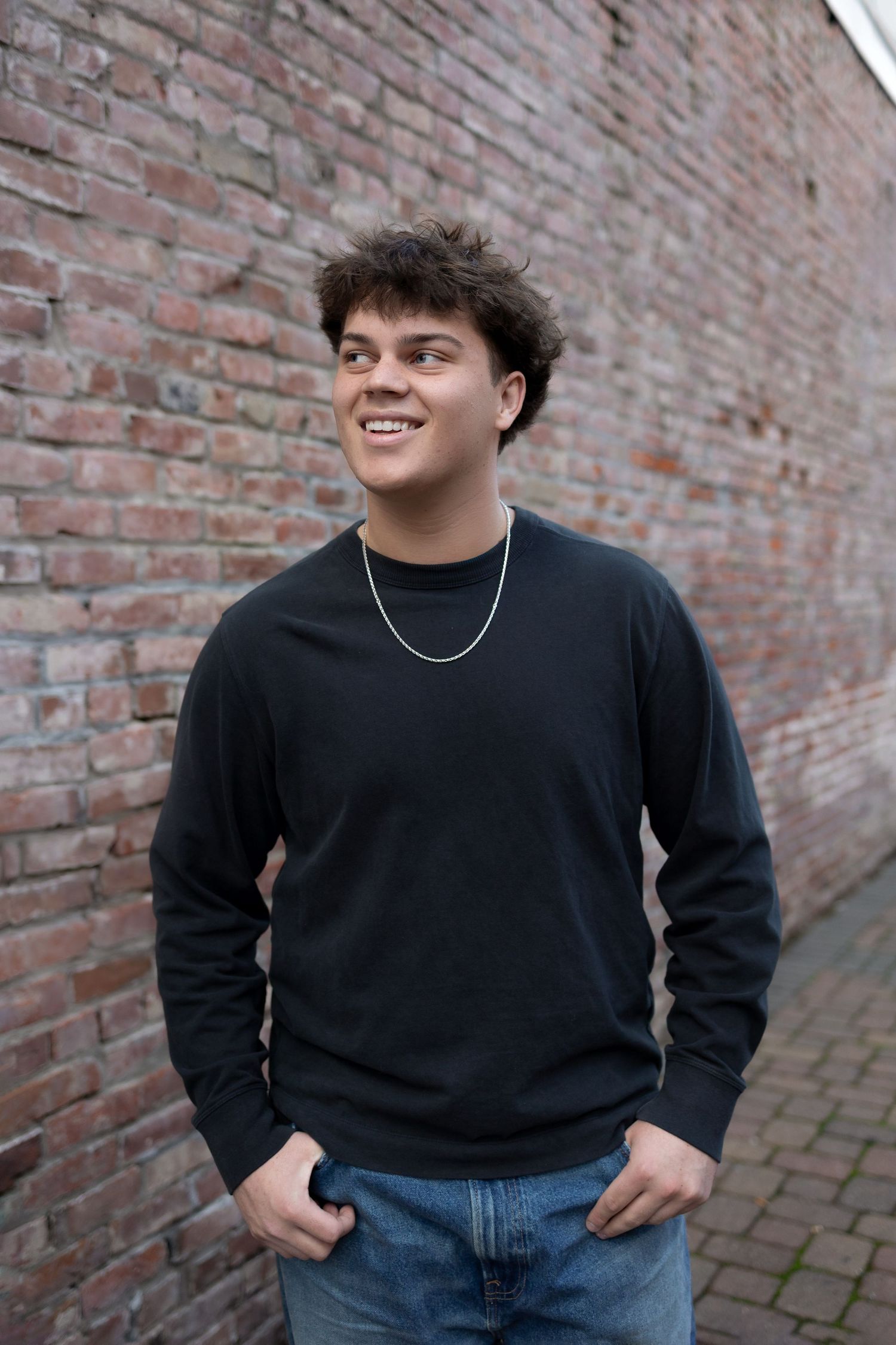 Vacaville teen guy leaning against red brick wall in a downtown alleyway with natural pose and warm sunset light
