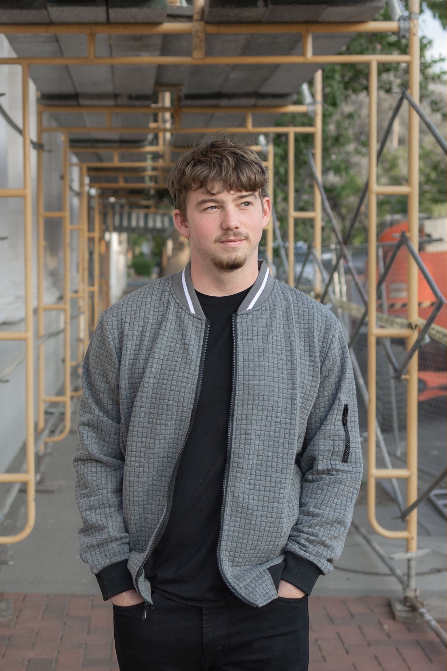 Male high school senior in bomber jacket standing beneath scaffolding in downtown Winters