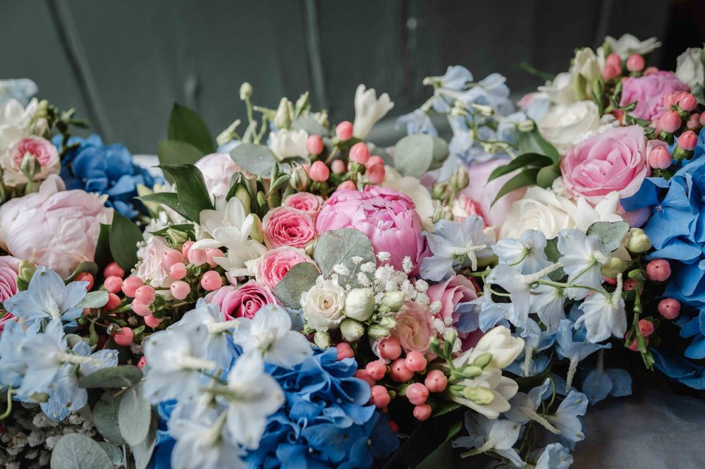 A romantic wedding bouquet with pink peonies, blue hydrangeas, and white flowers arranged in a natural style.