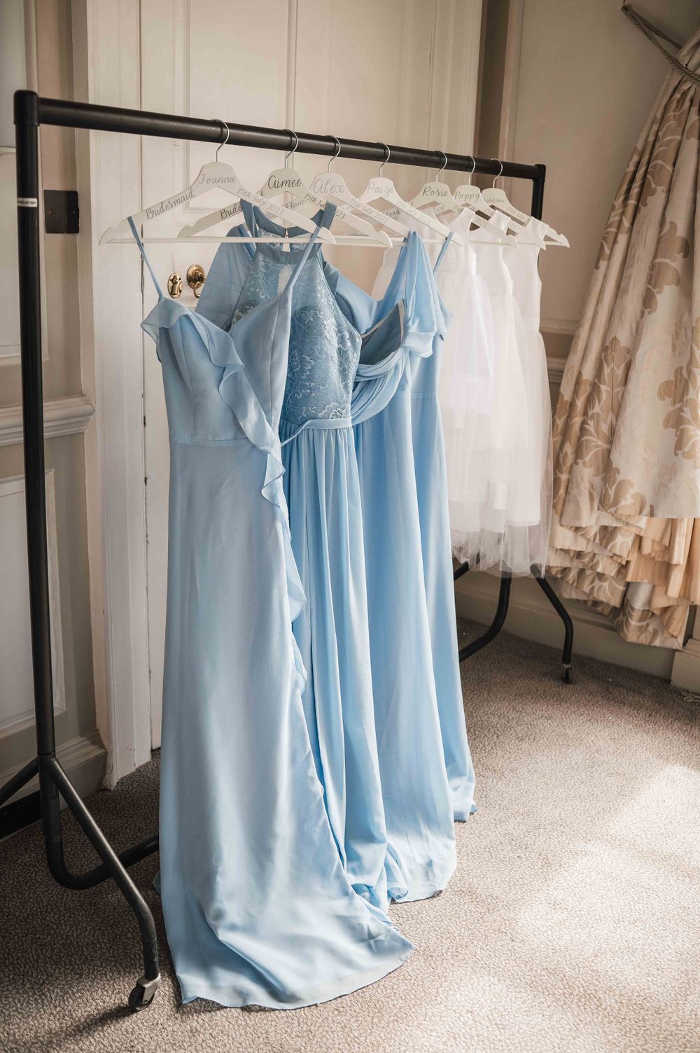 Light blue bridesmaid dresses hanging on a clothing rack next to white wedding dresses.