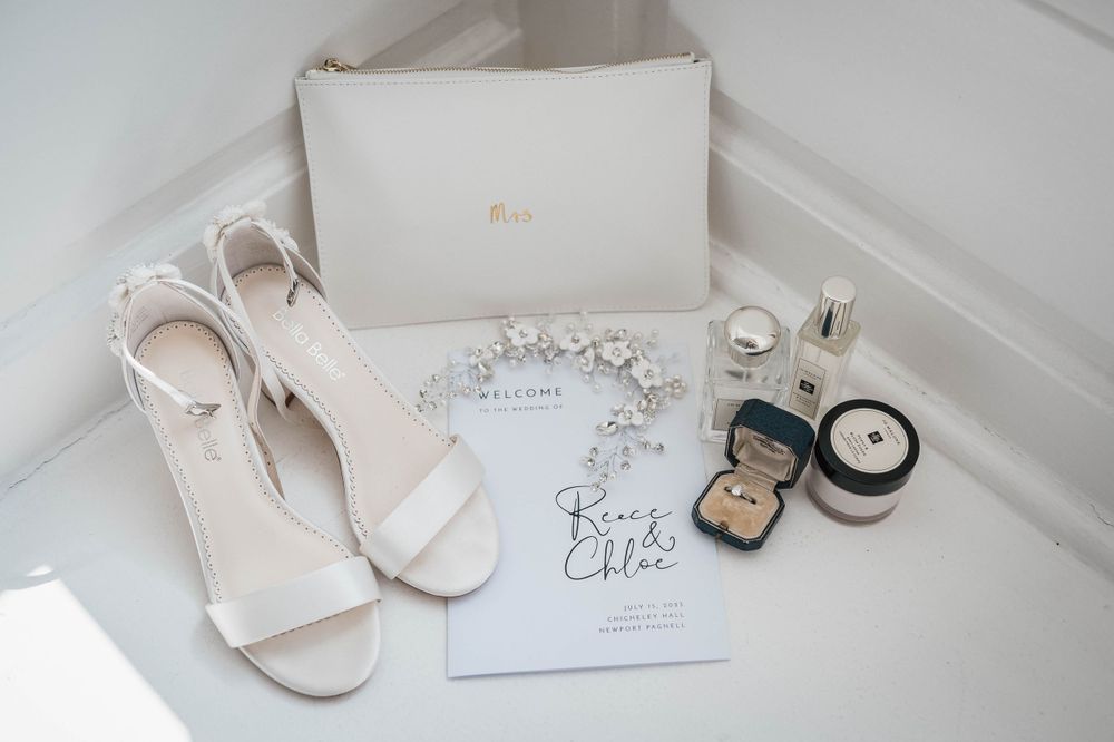 Wedding accessories including white shoes, jewelry, and invitations arranged on a white surface.