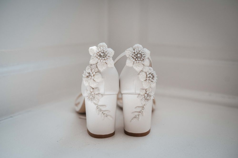 Elegant white bridal boots with delicate floral embellishments and beading displayed against a light background.