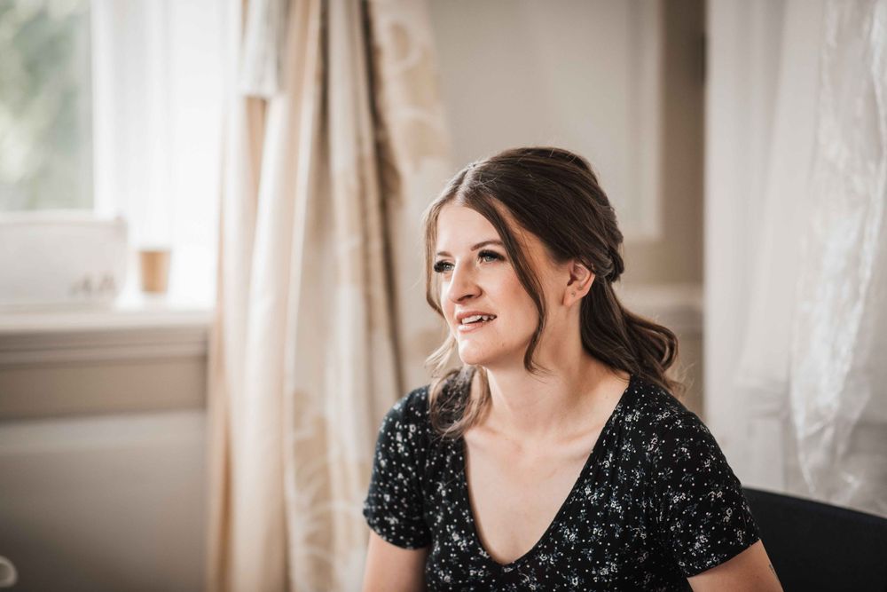 Person sitting by window wearing black floral dress in soft natural lighting.