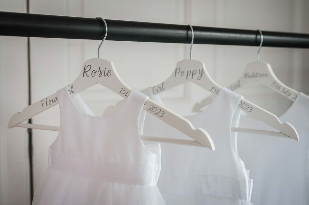 Three white wedding dresses hanging on personalized hangers against a dark curtain rod.