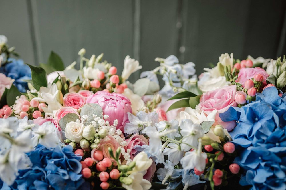 A romantic floral arrangement featuring blue hydrangeas, pink roses, and white flowers with delicate berries.