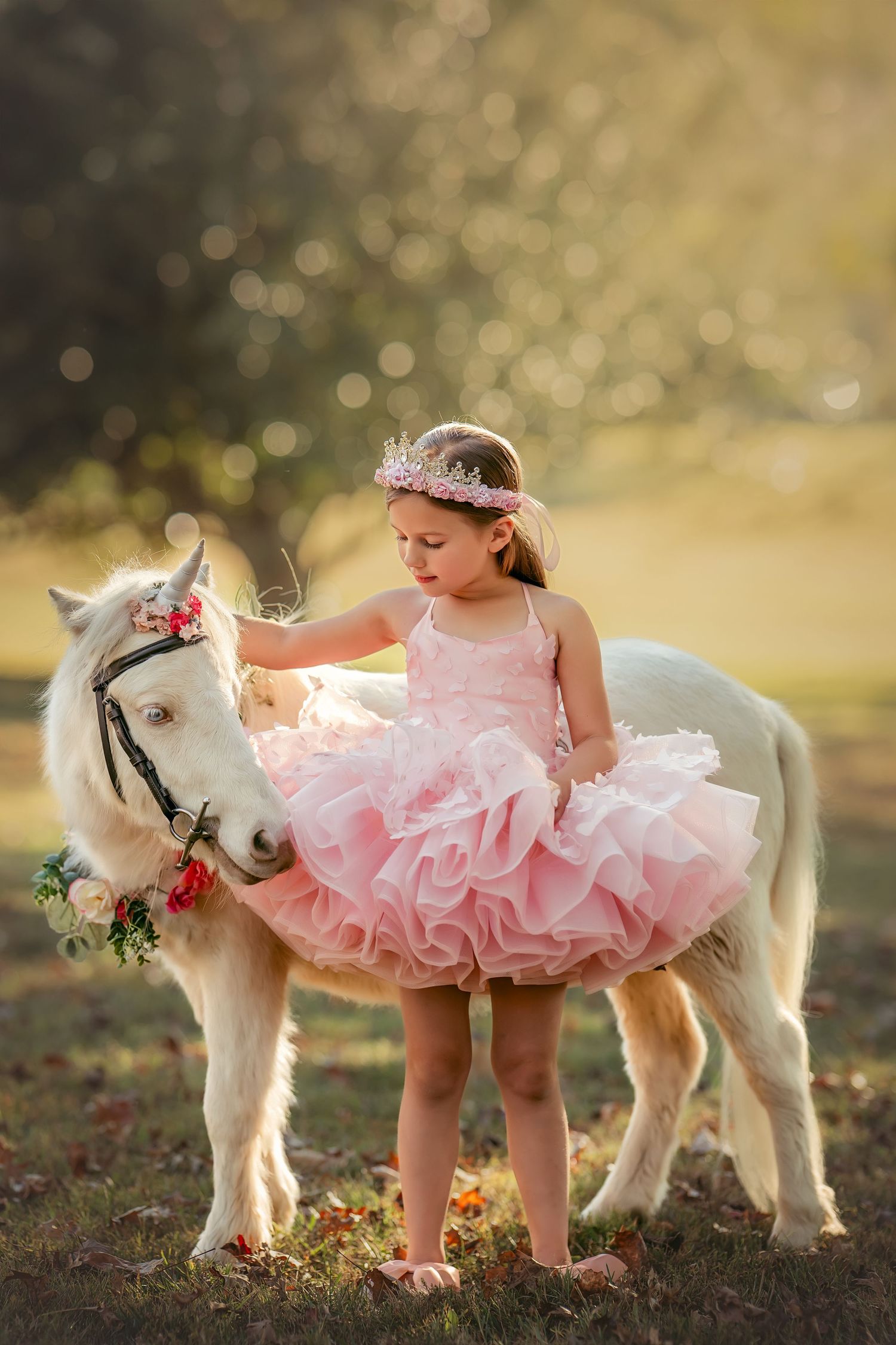 Young girl in pink tutu dress poses with a white pony unicorn at sunset.