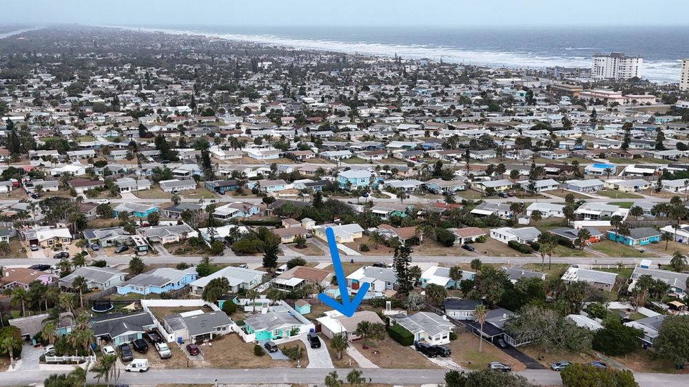 Wide aerial view of densely populated coastal community with blue marker indicating specific location.