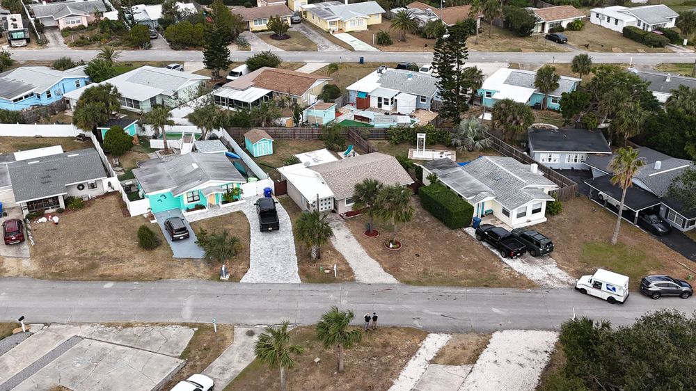 Aerial view of residential neighborhood with houses, pools and driveways visible.
