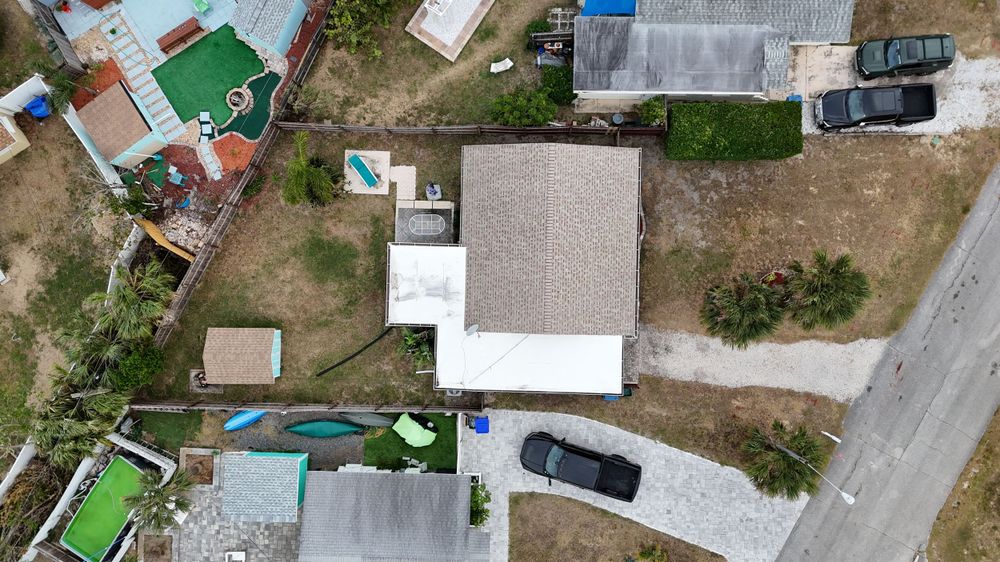 Drone shot of single family home with white roof, driveway and landscaped yard.