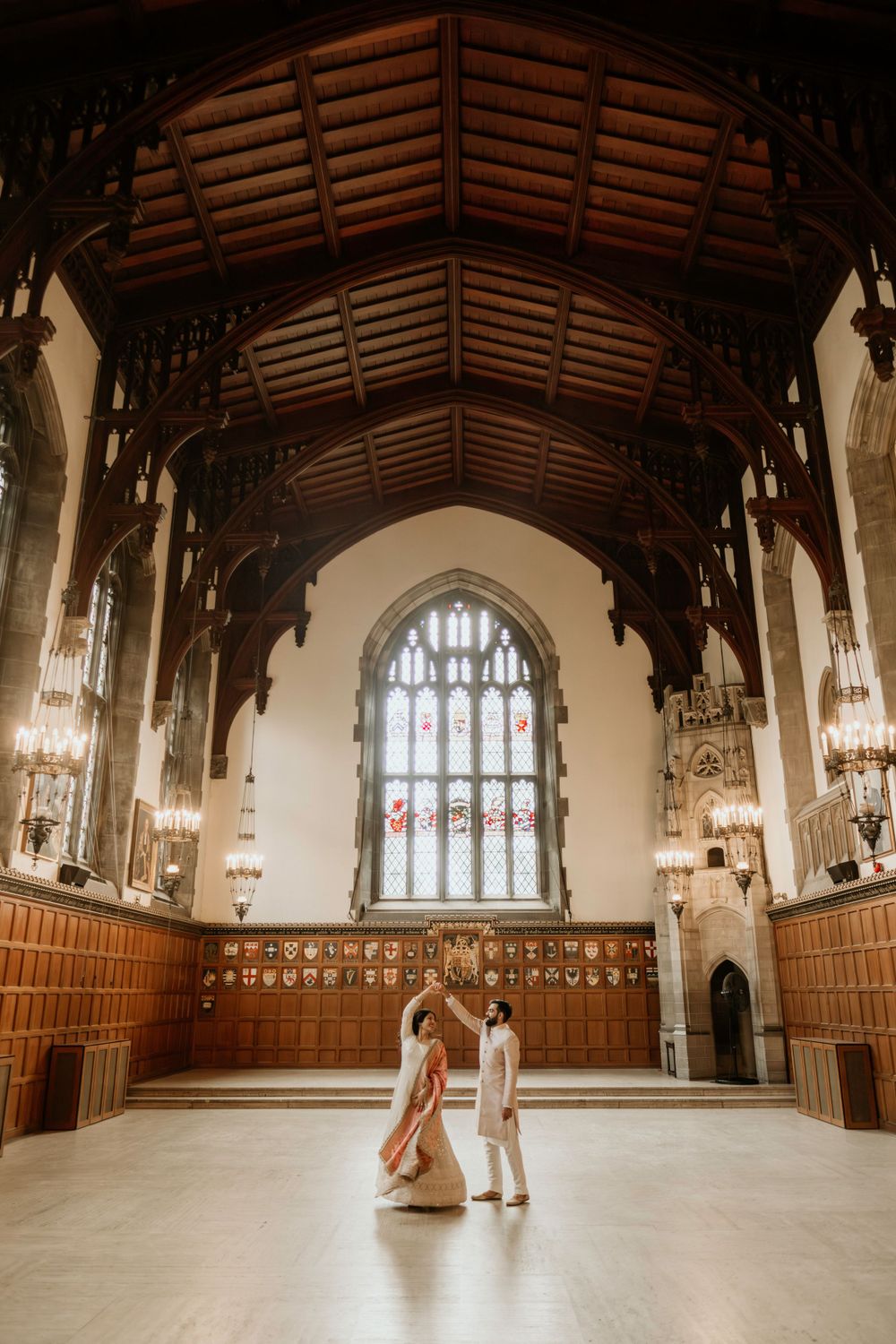 A romantic moment unfolds in a grand Gothic hall with wooden beams and a spectacular stained glass window.