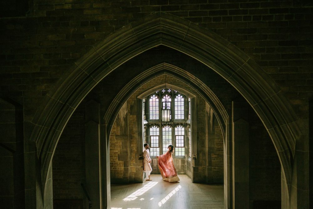 Figure in flowy gown stands beneath Gothic stone archway with sunlight streaming through stained glass windows.
