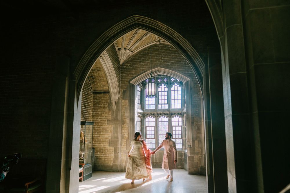 Two people holding hands in a grand Gothic stone archway with stained glass windows illuminating the historic interior.