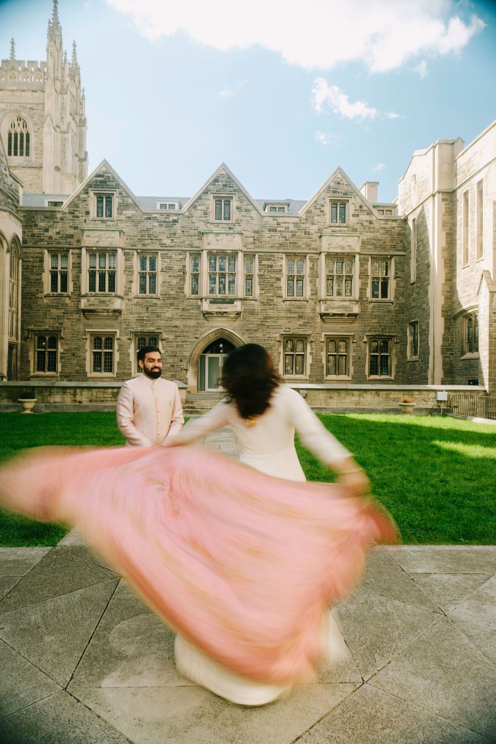 A couple dances in front of gothic university architecture as a pink dress twirls in motion.