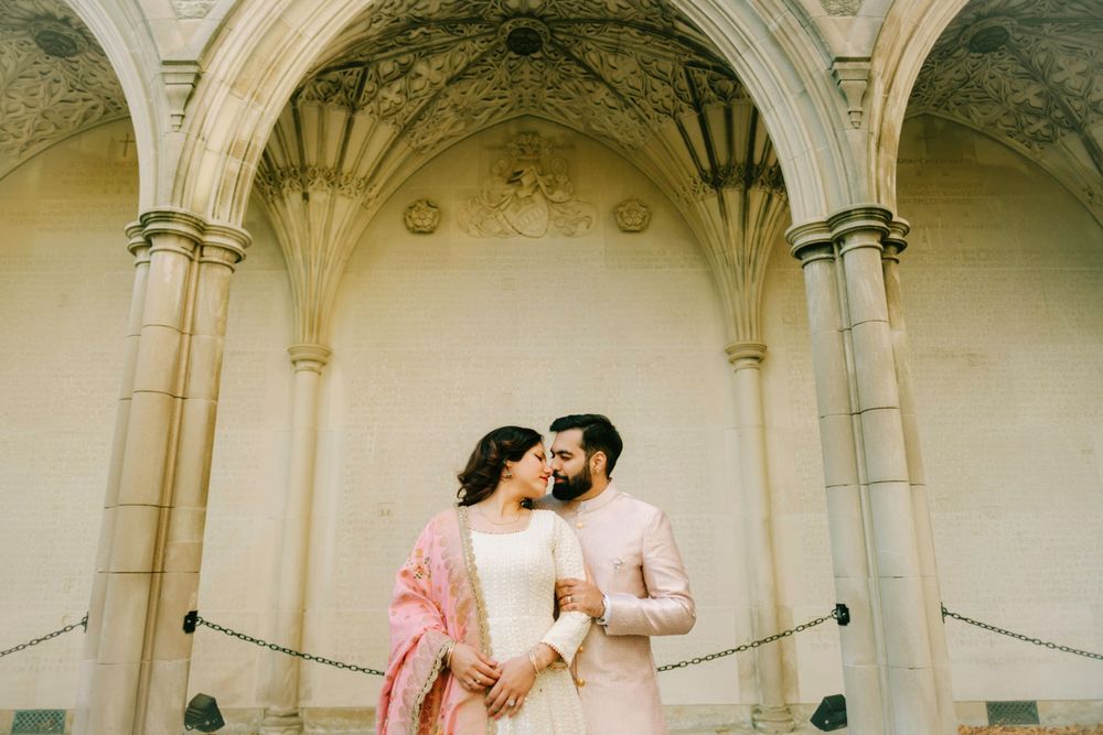A couple shares a tender moment under ornate stone archways with vaulted ceilings.