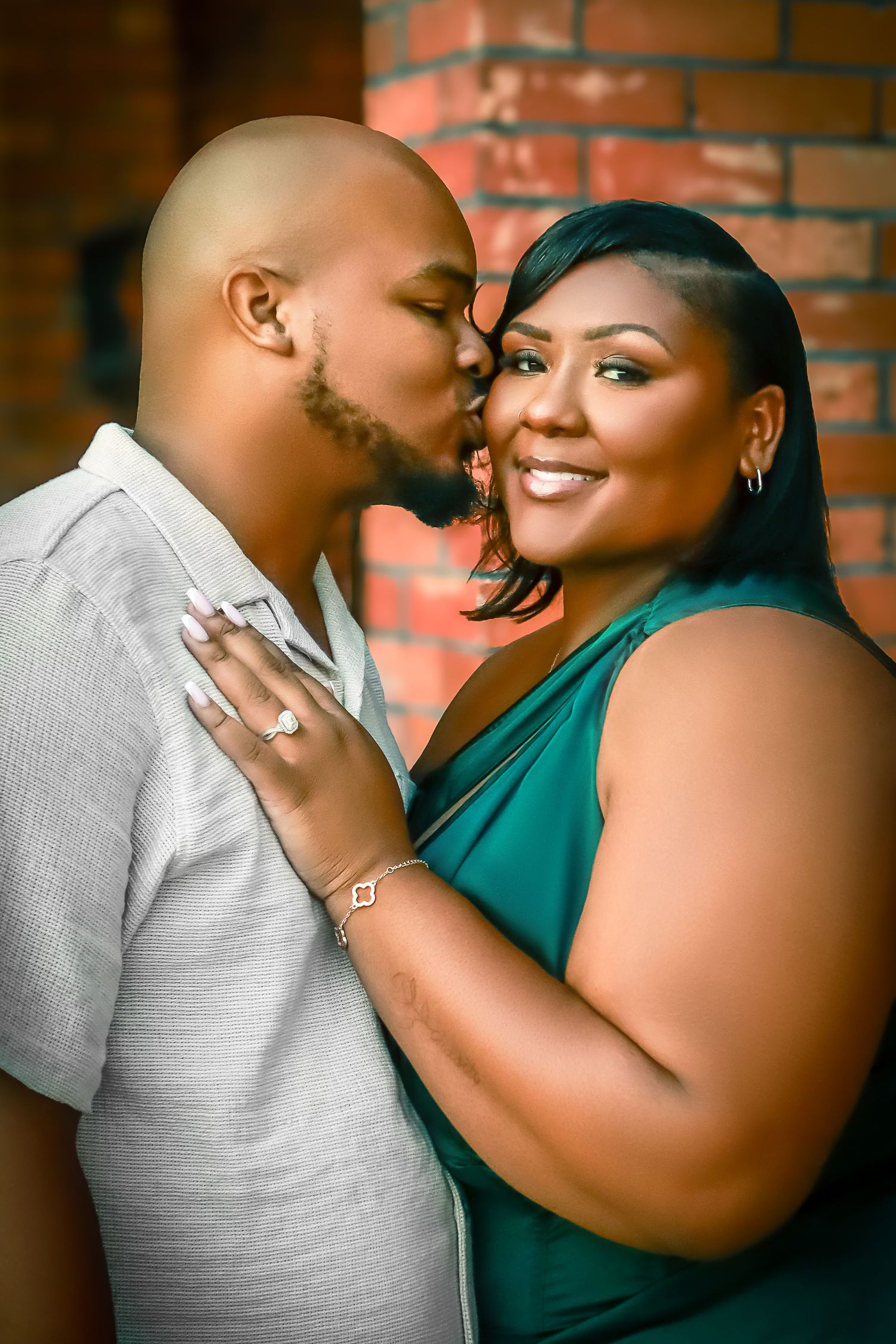 Romantic engagement portrait of a couple in coordinated outfits against a brick background.