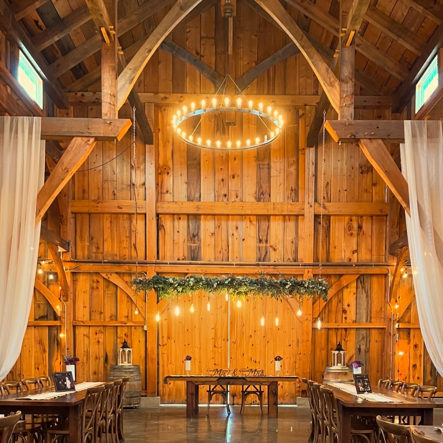 Rustic barn wedding venue with wooden beams and circular chandelier creating warm ambiance.