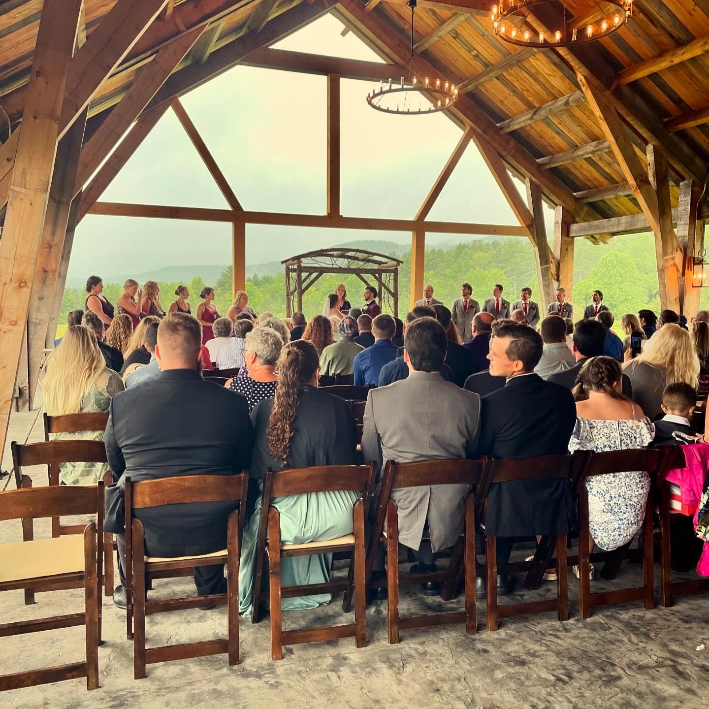 Wedding ceremony taking place in a rustic barn with exposed wooden beams and natural lighting.
