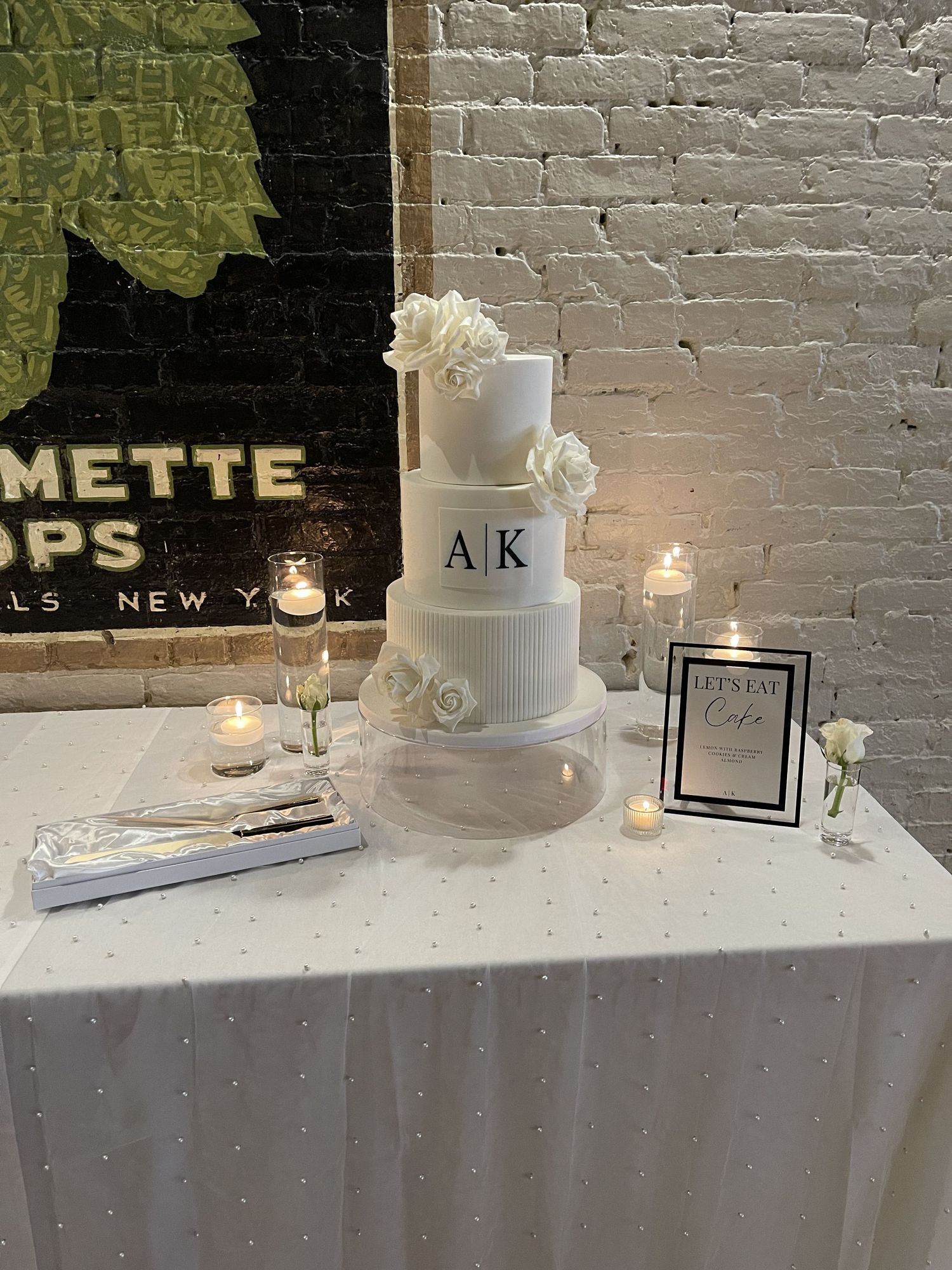 Elegant white wedding cake with monogram and floral decorations surrounded by candlelight.
