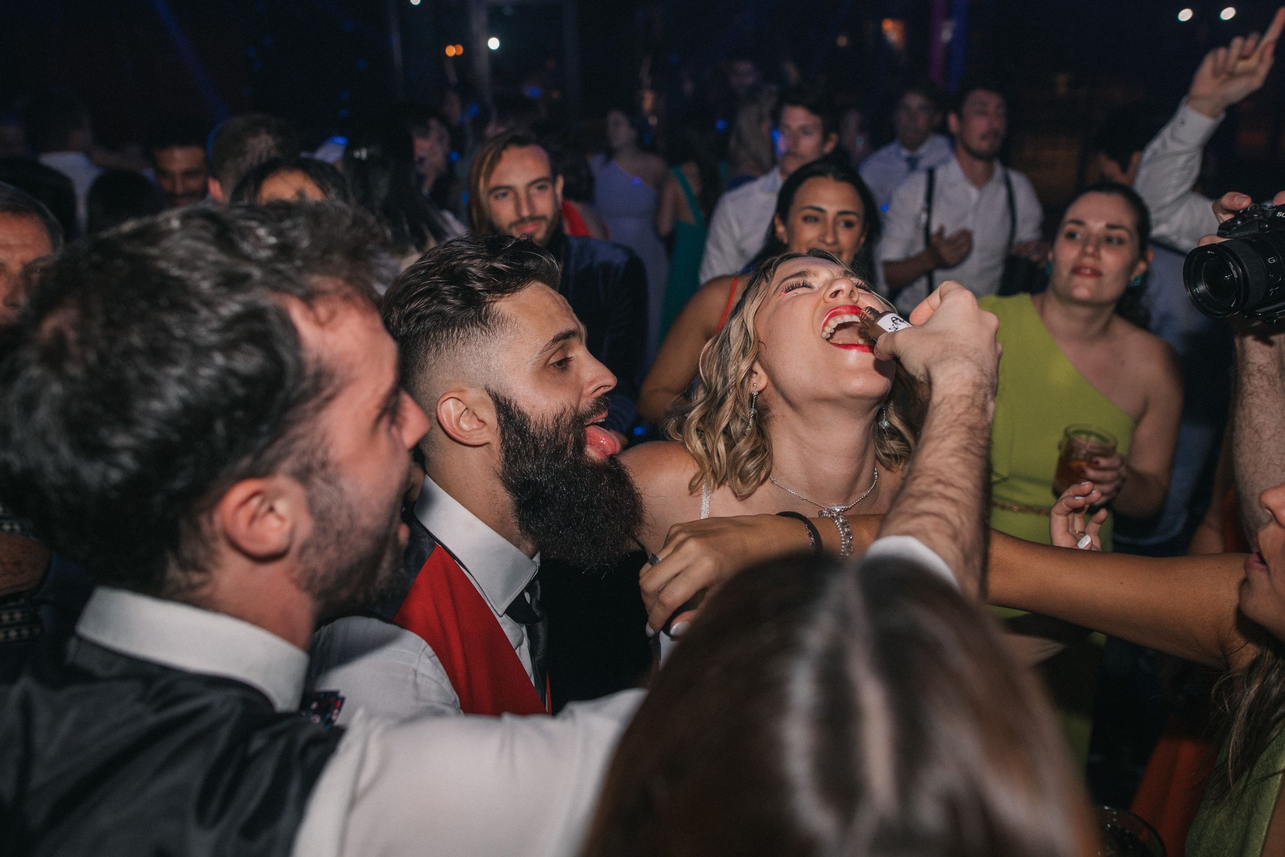 A crowded nightclub scene shows people enthusiastically singing and dancing together during a lively celebration.