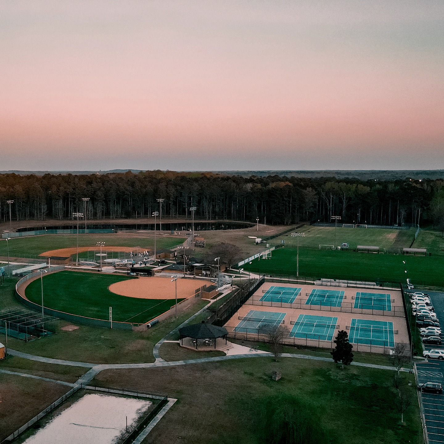 Aerial view of sports complex with baseball diamonds, tennis courts and athletic fields at dusk.