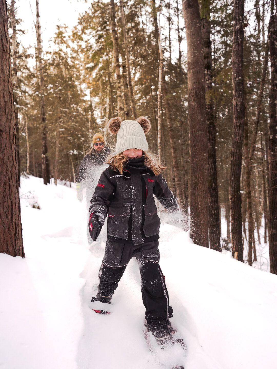 People playing and throwing snow in a wintry forest landscape.